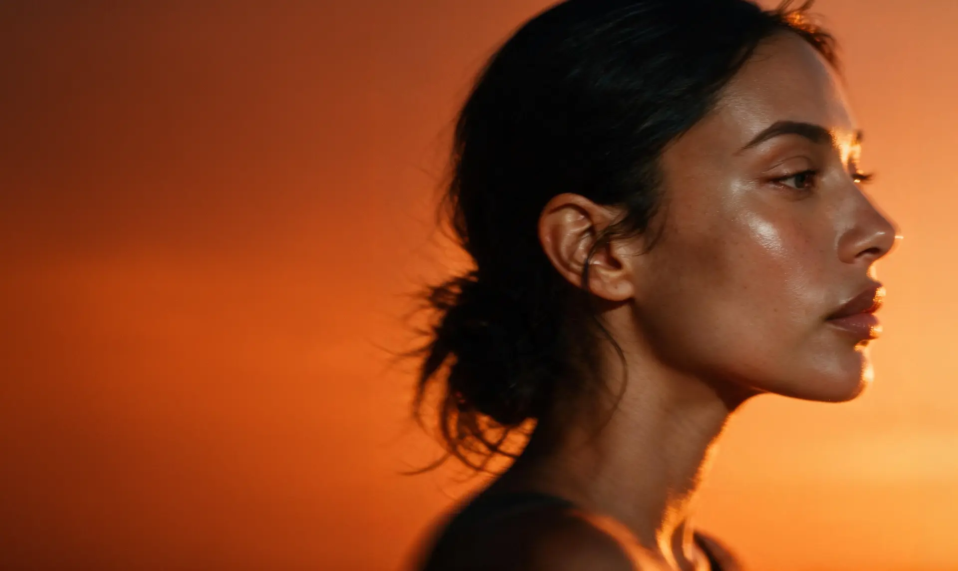Profile portrait of a woman with luminous skin against warm orange light